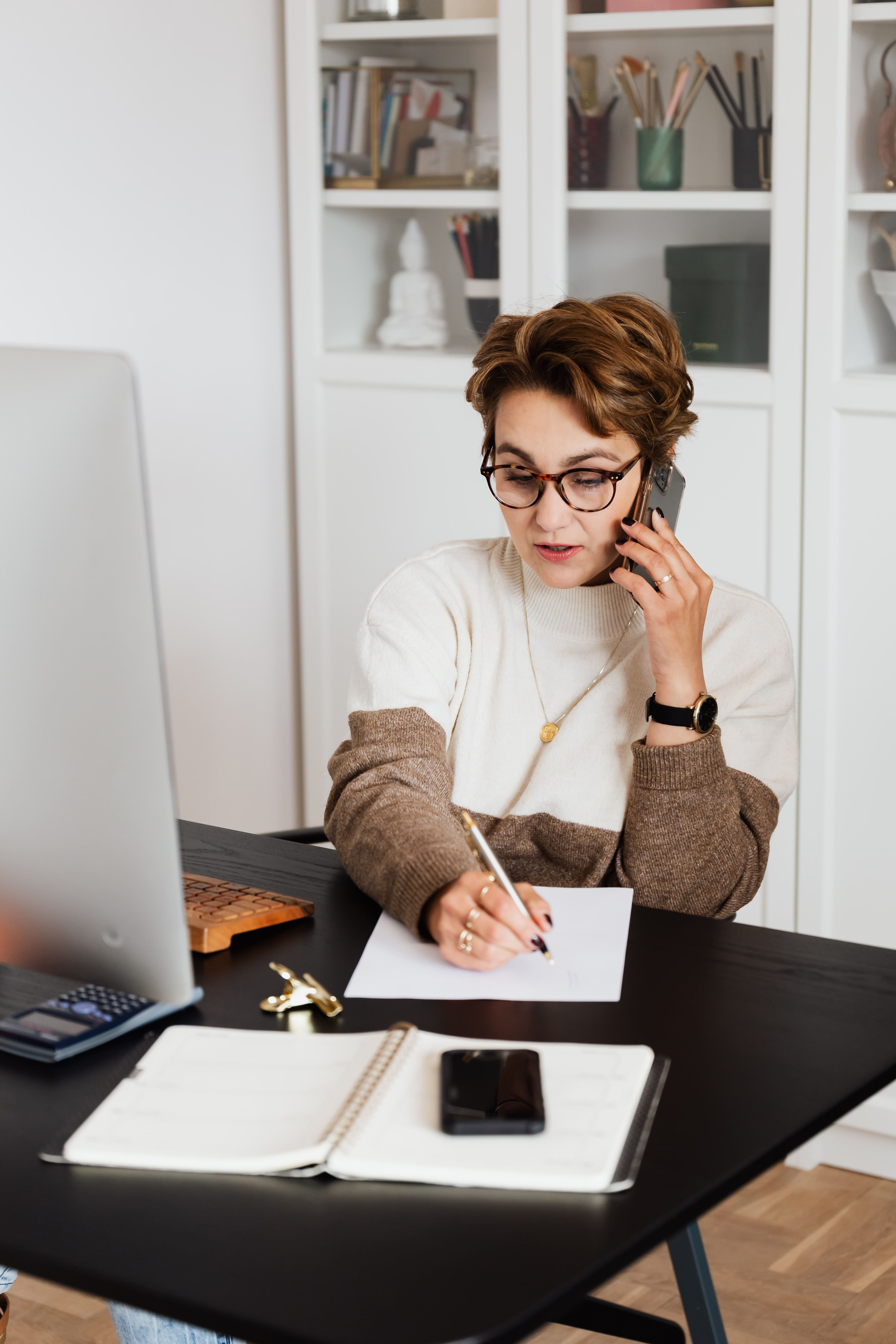 woman taking notes while talking on phone